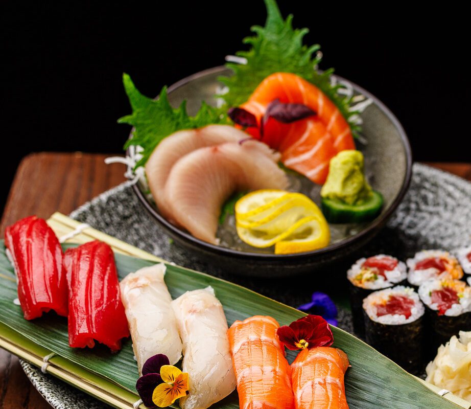 Assorted sushi and sashimi platter featuring various types of fish, including salmon, tuna, and white fish, served with rice, seaweed, and edible flowers