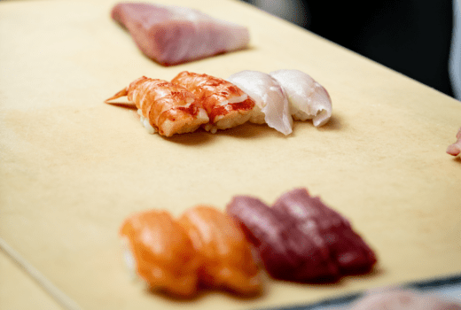 A close-up of various types of sushi, including shrimp nigiri, white fish nigiri, and salmon nigiri, arranged on a cutting board.