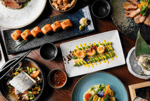 A table spread with a selection of Asian-inspired dishes, including sushi rolls, grilled meats, seafood, and vegetable dishes.